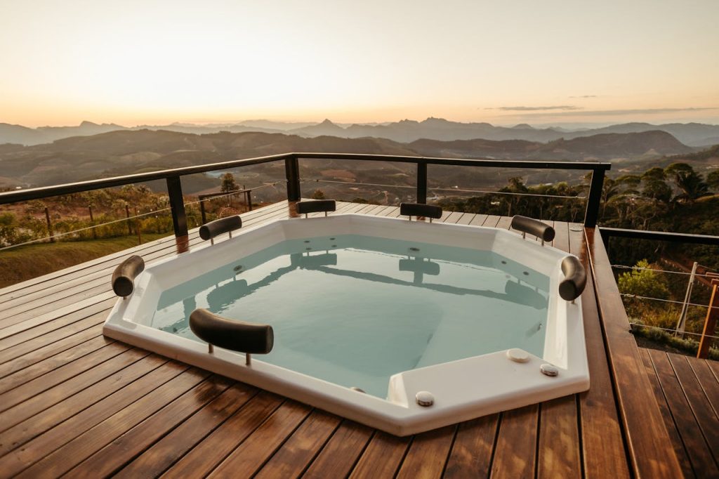 Large outdoor hot tub on a wooden deck, overlooking rolling hills and distant mountain views